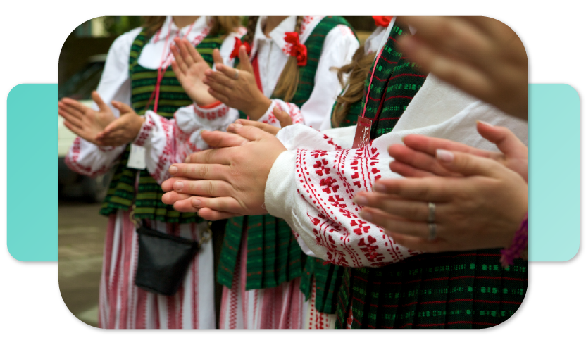 Grupė tautiškai apsirengusių ir plojančių žmonių.